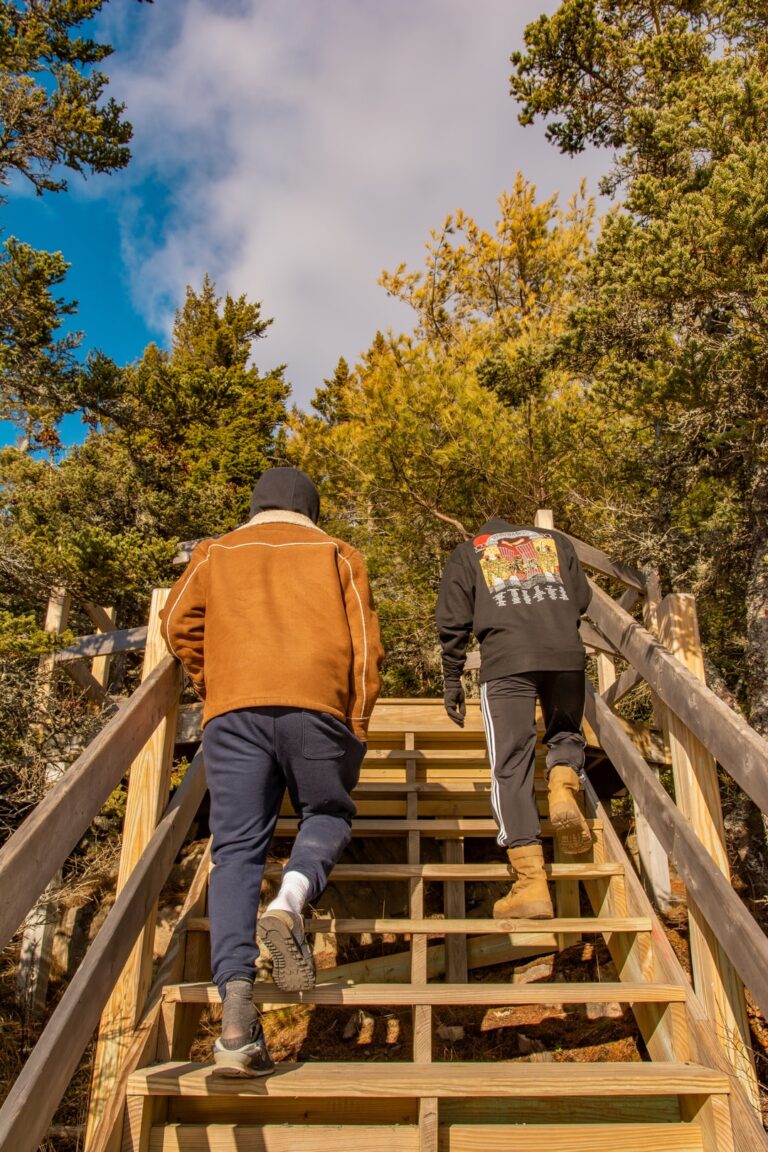 man in brown jacket and black pants walking on wooden bridge