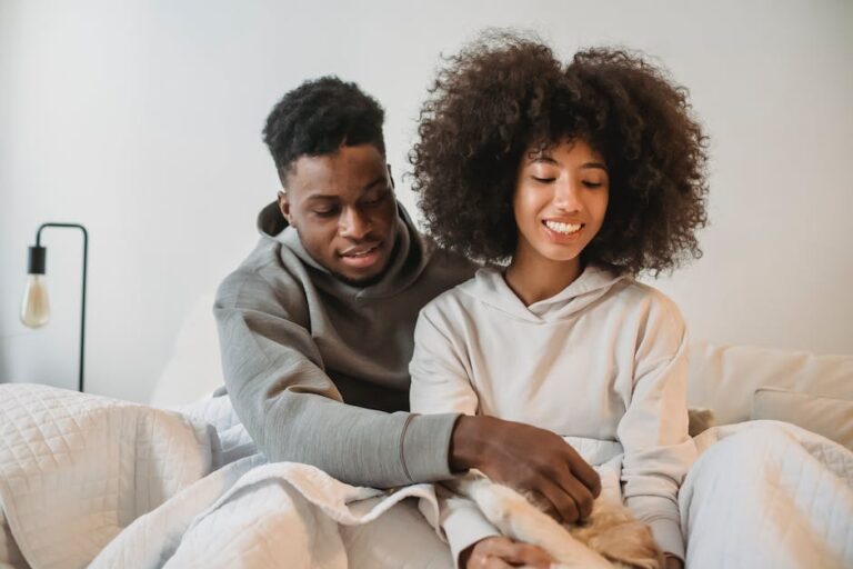 Young African American couple caressing cute little dog while resting in cozy bedroom